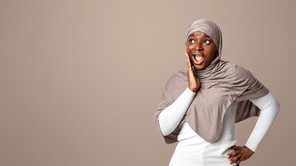 Shocking Offer. Surprised black islamic lady in hijab looking aside at copy space and touching face...