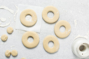 Overhead view of doughnut being cut out of dough, top view of doughnut dough on a white countertop, process of making doughnut