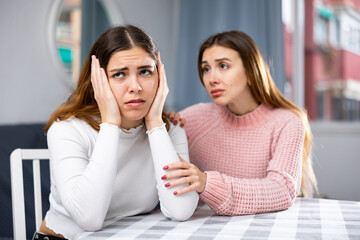 Worried young woman embracing, comforting and soothing female friend at home
