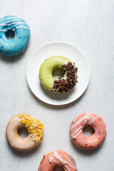 Overhead view of colorful glazed donuts on a white countertop, top view of homemade pastel doughnuts, process of making glazed doughnuts	
