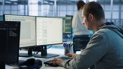 Engineer starting job shift in server hub used for processing vast amounts of data. IT programmer arriving at work in data center, sitting at PC desk, typing on keyboard, camera A