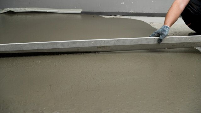 Construction worker smoothing liquid cement surface using a screed tool to achieve a flat and even finish