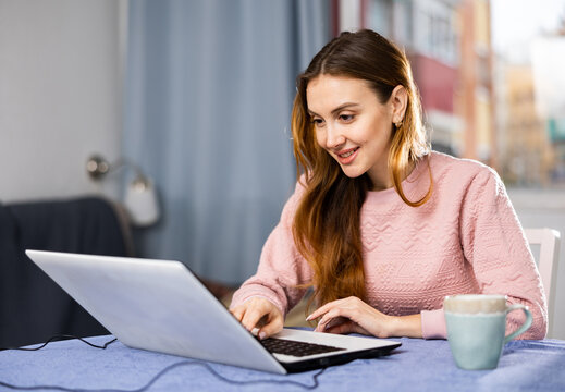 Portrait of young woman sitting at table in living room looking at laptop screen