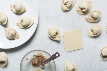 Overhead view of dumpling being wrapped, top view of wonton being filled, process of making homemade wontons