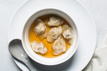 Overhead view of wonton soup in a white ceramic bowl, clear soup with dumplings in a white soup bowl