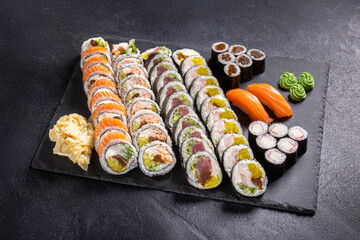 Assorted Sushi Platter with Rolls, Nigiri and Maki on Slate.
Variety sushi set including salmon rolls, tuna rolls, nigiri and maki, served with wasabi, ginger and soy sauce on black slate plate.