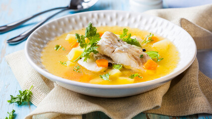 Fresh fish soup served in a bowl garnished with herbs and vegetables on a rustic table.