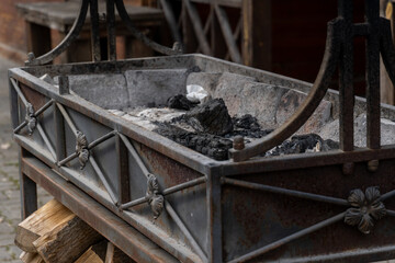 Rustic metal fire pit with burned logs and wood storage underneath displaying signs of age and weathered use.