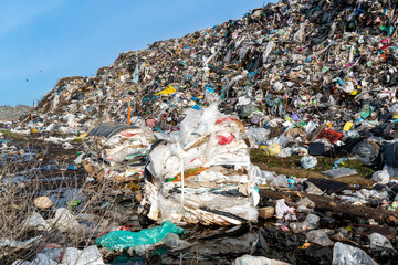 Vast landfill shows accumulation of garbage and waste products, with a clear blue sky, and...