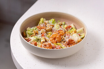 Caesar Salad with Grilled Shrimp, Croutons and Parmesan.
Fresh Caesar salad with grilled shrimp, cherry tomatoes, crunchy croutons and shredded Parmesan in a white bowl.