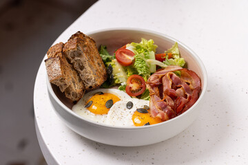 Breakfast Bowl with Eggs, Bacon, Salad and Bread.
Balanced breakfast bowl featuring sunny-side-up eggs, crispy bacon, fresh salad, cherry tomatoes, and rustic bread slices.
