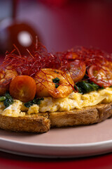 Open Sandwich with Scrambled Eggs, Shrimp and Chili Threads.
Gourmet toast topped with scrambled eggs, sautéed shrimp, spinach and red chili threads, served on a pastel plate.