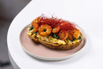 Open Sandwich with Scrambled Eggs, Shrimp and Chili Threads.
Gourmet toast topped with scrambled eggs, sautéed shrimp, spinach and red chili threads, served on a pastel plate.