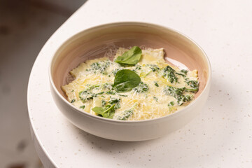 Spinach Ravioli with Creamy Parmesan Sauce.
Fresh ravioli pasta filled with spinach, topped with creamy cheese sauce and garnished with spinach leaves in a modern bowl.