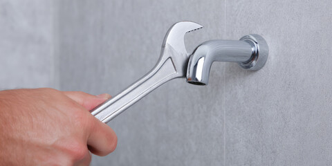 A hand uses a wrench to tighten a faucet on a wall. Home repair and plumbing maintenance