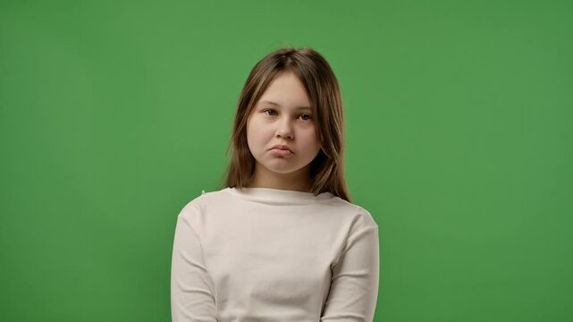 Teenage girl posing at camera with sad upset pouting face, negative expression, isolated on chroma key green screen studio background mockup. Slow motion