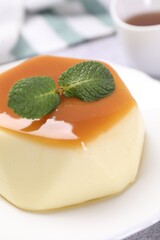 Delicious pudding with caramel sauce and mint on light table, closeup