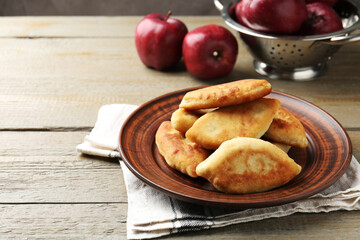 Delicious fried pyrizhky (stuffed pies) with apples on wooden table. Space for text