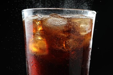 Refreshing cola and ice cubes in glass on black background, closeup