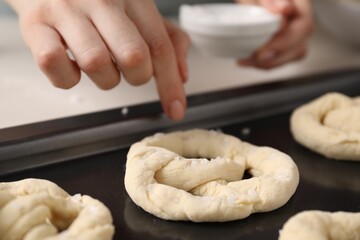 Woman putting salt onto raw pretzels at white table, closeup