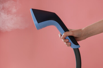 Woman with clothes steamer on pink background, closeup