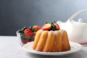 Tasty Bundt cake with powdered sugar and berries on light grey table, closeup