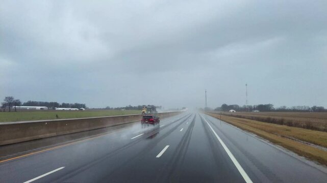 A truck drives through heavy rain on the highway, with water splashing from the tires and visibility reduced by the intense downpour. The scene emphasizes determination and the challenges of driving i