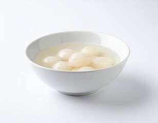 Bowl containing several white lychee fruits submerged in a clear liquid, against a white backdrop