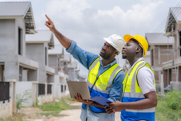 African male engineer supervising building construction with construction workers who are inspecting and planning the work on a laptop.
