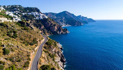 Coastal road winds beside the ocean beneath a hill covered with white buildings