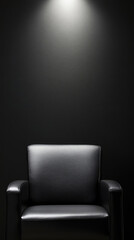 A single black leather armchair sits centrally illuminated against a dark wall