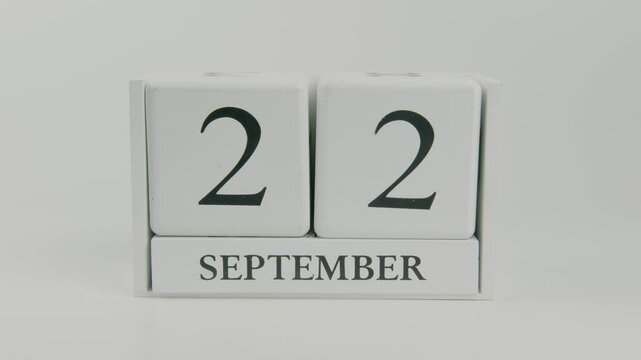 A hand flips a wooden calendar from September 22nd to September 23rd on a white background, marking the transition to the next day