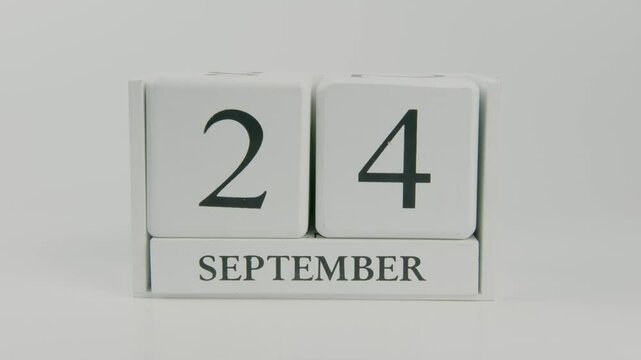 A hand flips a wooden calendar from September 24th to September 25th on a white background, marking the change in the day