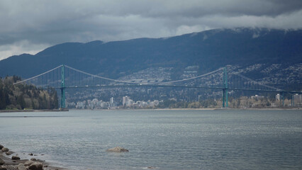 Lions Gate Bridge in Vancouver, British Columbia on a cloudy day with mountains and city in...