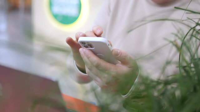 Person is holding a cell phone and looking at it. The phone is an iPhone. The person is in a green and white environment