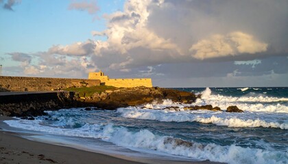 Coastal fortification overlooking the sea, waves crashing on rocks under cloudy sky