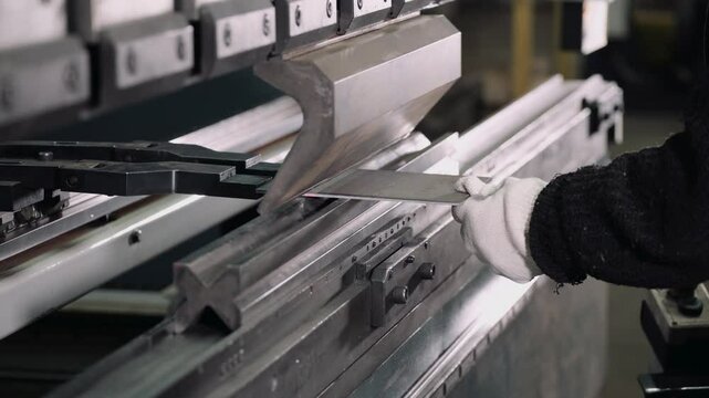 Employee inserts metal into bending machine tool in workshop