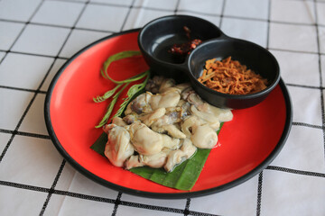 Fresh Oysters serve with spicy sauce and fried garlic in red-black plate on the table.