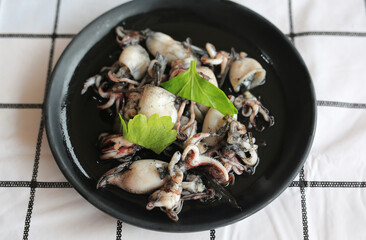 Stir fry squid in black squid ink sauce in black plate on table. Thai Seafood menu. Close up shot.