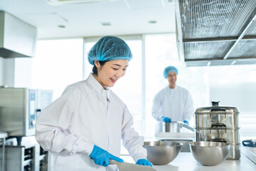 厨房で料理する衛生白衣を着た女性調理師　給食センター　給食室