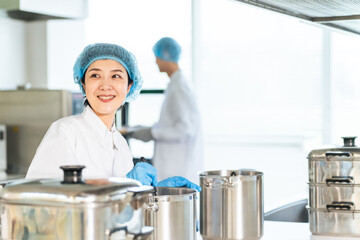 厨房で大鍋で調理する衛生白衣を着た女性調理師　給食センター　給食室