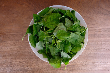 White bowl full of fresh green spinach leaves ready to cook