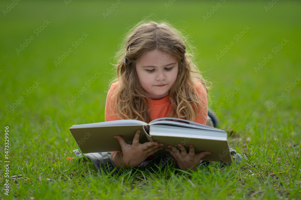 Poster child reading a book in the grass. child enjoying a book story outdoors. child studying with book in