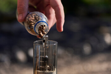 Coffee grinding process: close up view of a hand pouring roasted beans into a grinder, outdoors on...