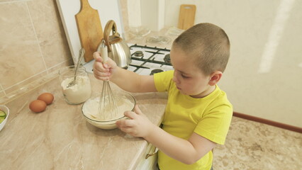 A child is engaging in cooking activity in the kitchen while using a whisk and a bowl effectively