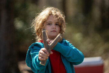 Slingshot in kids hand. Kid holding catapult. Kid aiming with sling. Funny kid playing with...
