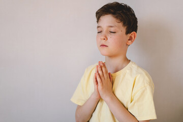 A boy with folded hands in front of him, he is praying or meditating. Concept of Christianity, religion and faith.