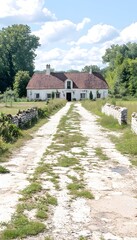 Fototapeta premium A white farmhouse with a red tile roof sits at the end of a long, gravel driveway lined with stone walls