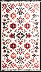 A white rug with a symmetrical pattern of red, black, and grey floral motifs
