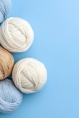 Five balls of yarn in blue, white, and beige shades against a light blue background, creating a minimalist and inviting visual